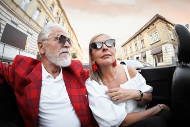 Photo of Senior couple enjoying cabriolet ride in city, wide angle lens