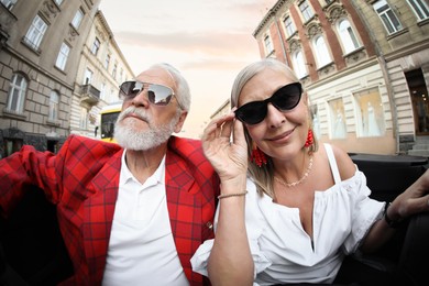 Photo of Senior couple enjoying cabriolet ride in city, wide angle lens