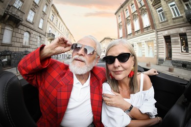 Photo of Senior couple enjoying cabriolet ride in city, wide angle lens