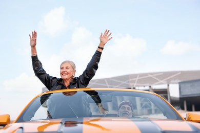 Photo of Senior couple enjoying cabriolet ride in city. Woman with wide open arms