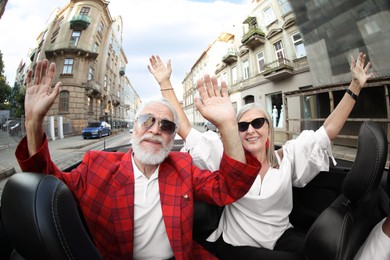 Photo of Senior couple enjoying cabriolet ride in city, wide angle lens
