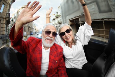 Photo of Senior couple enjoying cabriolet ride in city, wide angle lens