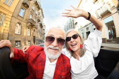 Photo of Senior couple enjoying cabriolet ride in city, wide angle lens