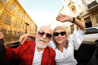 Photo of Senior couple enjoying cabriolet ride in city, wide angle lens