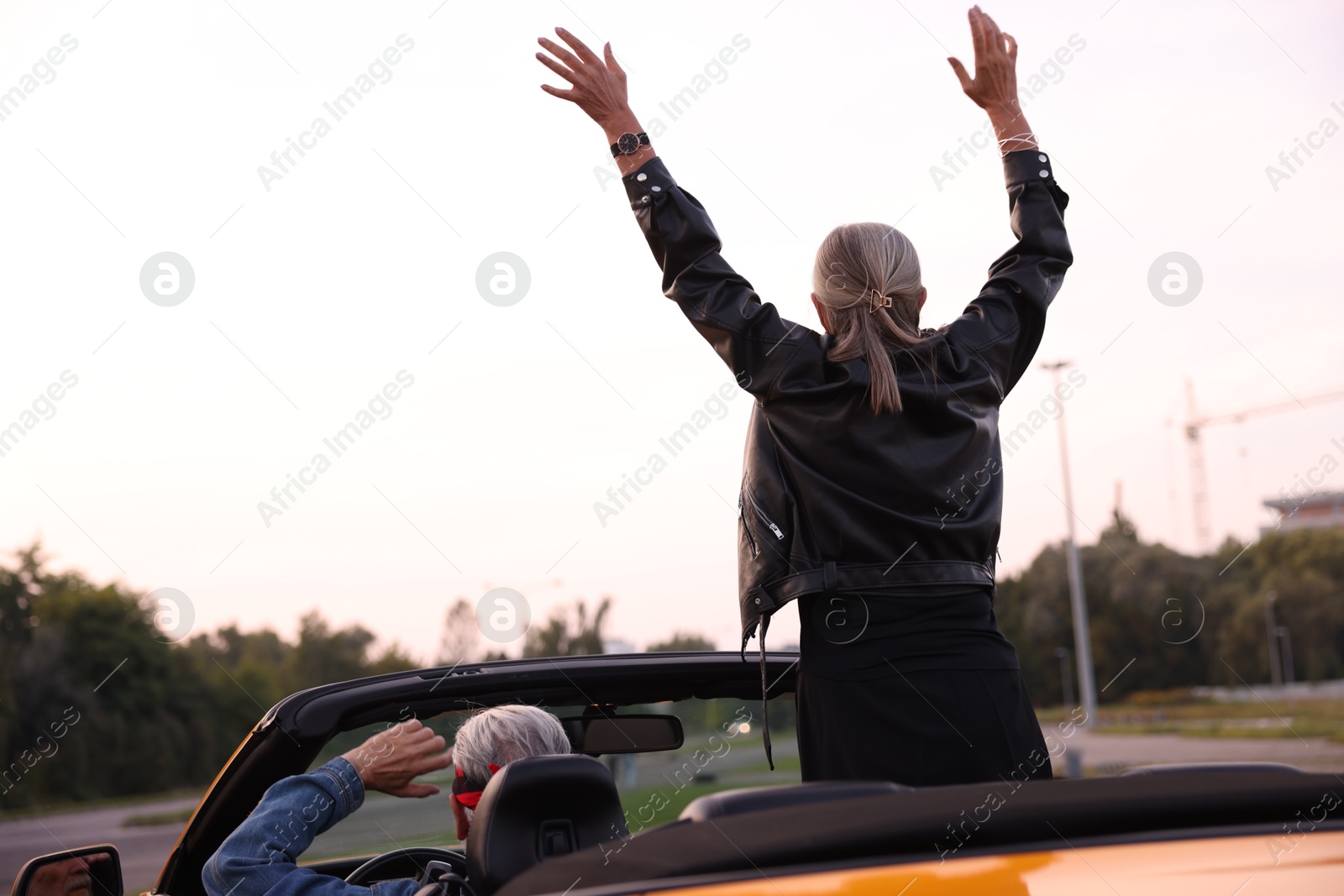 Senior couple enjoying cabriolet ride in city, back view. Woman with wide open arms Photo of Senior couple enjoying cabriolet ride in city, back view. Woman with wide open arms