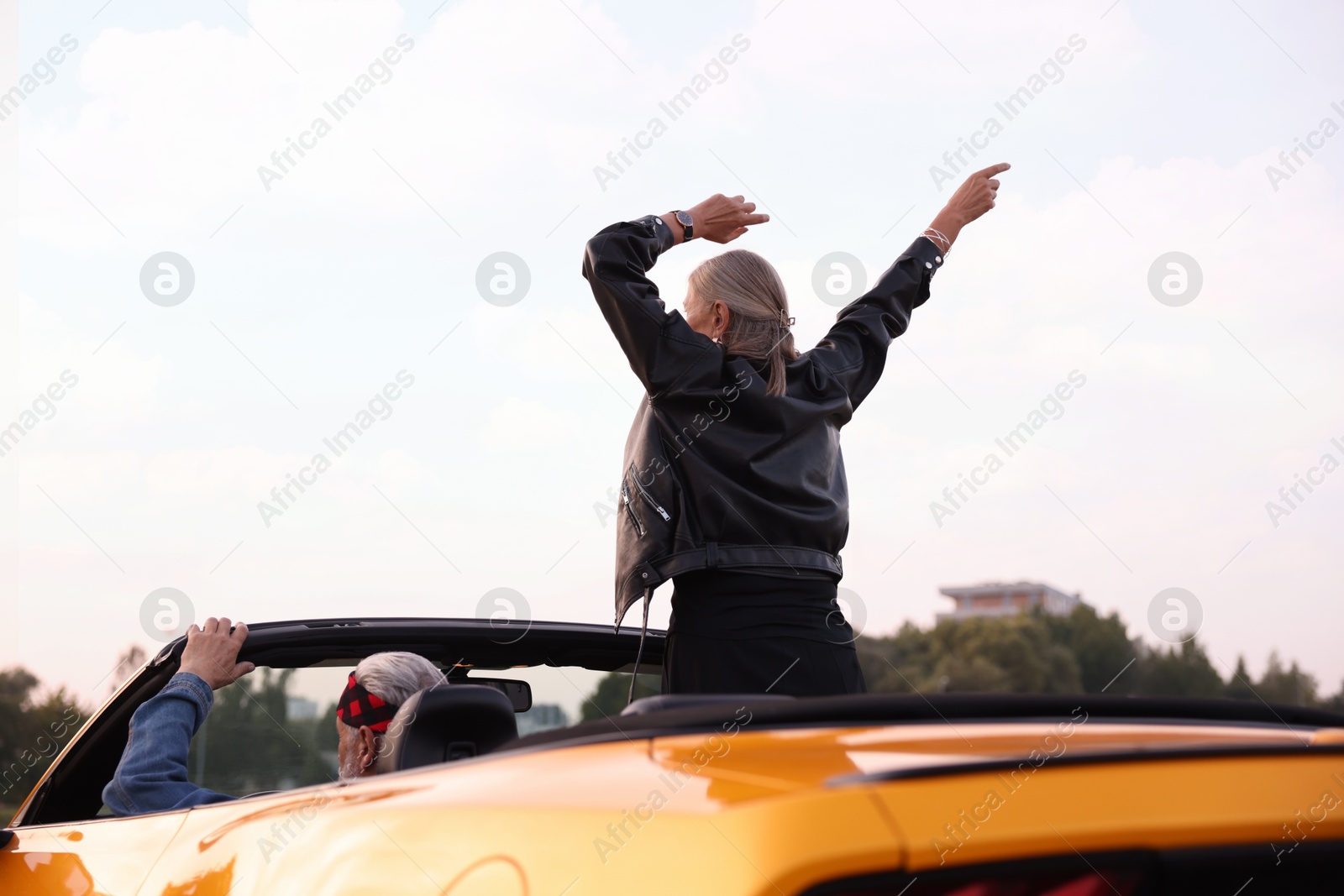 Photo of Senior couple enjoying cabriolet ride in city, back view. Woman with wide open arms