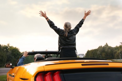 Photo of Senior couple enjoying cabriolet ride in city, back view. Woman with wide open arms