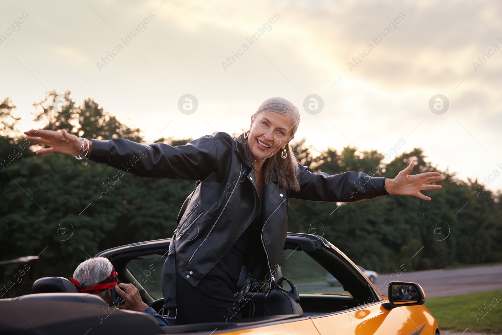 Photo of Senior couple in modern cabriolet outdoors. Woman with wide open arms and man talking on phone