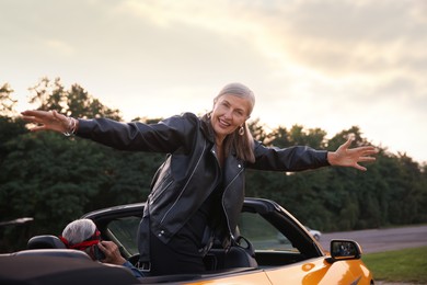 Photo of Senior couple in modern cabriolet outdoors. Woman with wide open arms and man talking on phone