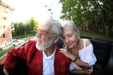 Photo of Senior couple enjoying cabriolet ride in city, wide angle lens