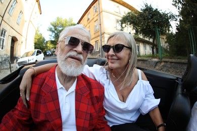 Photo of Senior couple enjoying cabriolet ride in city, wide angle lens