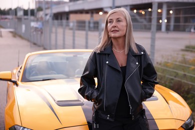 Photo of Stylish senior woman near modern cabriolet outdoors