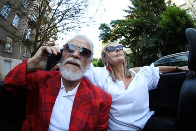 Photo of Senior woman and man talking on phone while enjoying cabriolet ride in city, wide angle lens