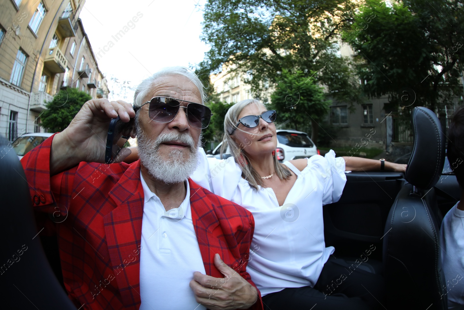 Photo of Senior woman and man talking on phone while enjoying cabriolet ride in city, wide angle lens