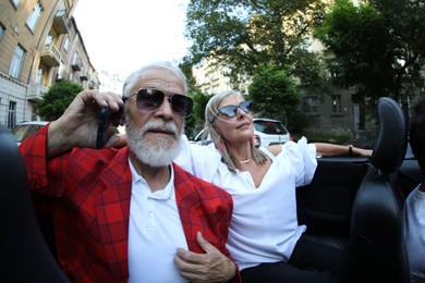 Photo of Senior woman and man talking on phone while enjoying cabriolet ride in city, wide angle lens