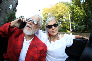Photo of Senior woman and man talking on phone while enjoying cabriolet ride in city, wide angle lens