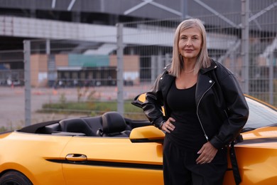 Photo of Stylish senior woman near modern cabriolet outdoors. Space for text