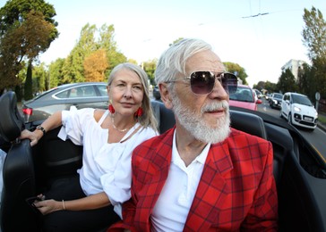 Photo of Senior couple enjoying cabriolet ride in city, wide angle lens