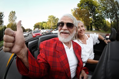 Photo of Senior couple enjoying cabriolet ride in city, wide angle lens