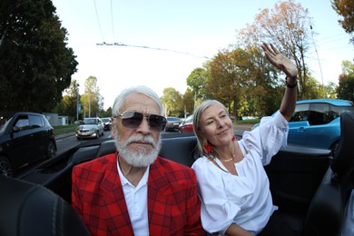 Photo of Senior couple enjoying cabriolet ride in city, wide angle lens