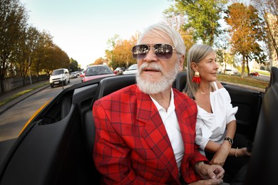 Photo of Senior couple enjoying cabriolet ride in city, wide angle lens