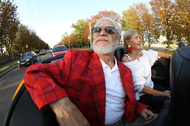 Photo of Senior couple enjoying cabriolet ride in city, wide angle lens