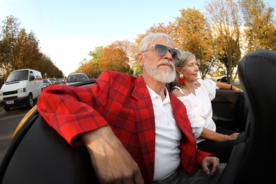 Photo of Senior couple enjoying cabriolet ride in city, wide angle lens