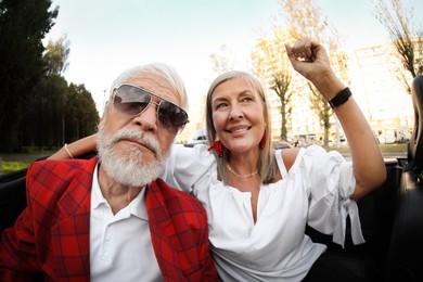 Photo of Senior couple enjoying cabriolet ride in city, wide angle lens