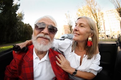 Photo of Senior couple enjoying cabriolet ride in city, wide angle lens