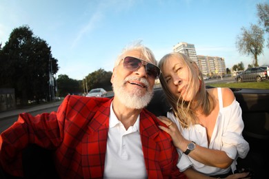 Photo of Senior couple enjoying cabriolet ride in city, wide angle lens