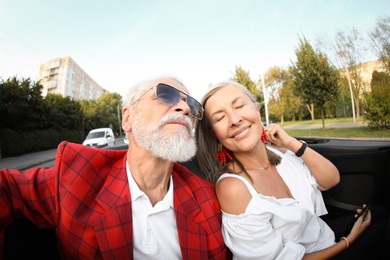 Photo of Senior couple enjoying cabriolet ride in city, wide angle lens
