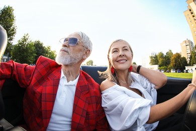 Photo of Senior couple enjoying cabriolet ride in city, wide angle lens