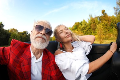Photo of Senior couple enjoying cabriolet ride outdoors, wide angle lens