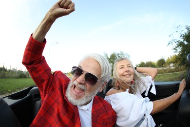 Photo of Senior couple enjoying cabriolet ride outdoors, wide angle lens
