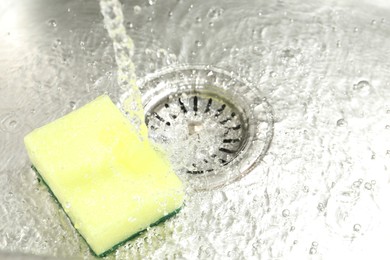 Photo of Water going down drain and sponge in sink, closeup