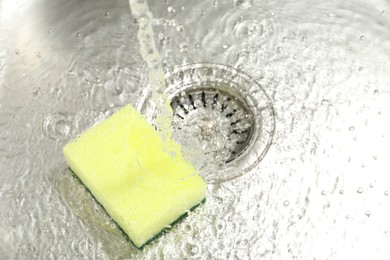 Photo of Water going down drain and sponge in sink, closeup