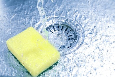 Photo of Water going down drain and sponge in sink, closeup