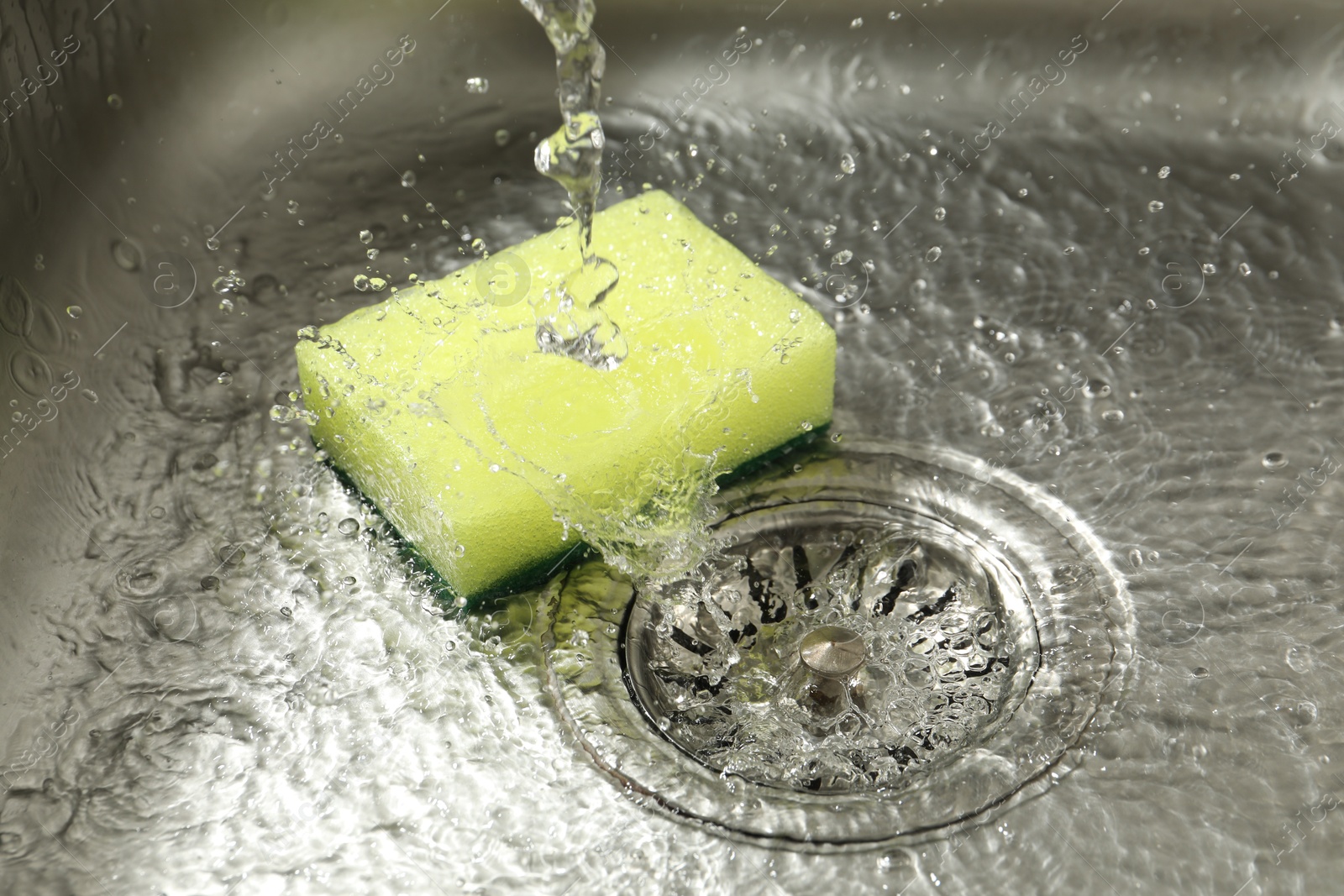 Water going down drain and sponge in sink, closeup Photo of Water going down drain and sponge in sink, closeup