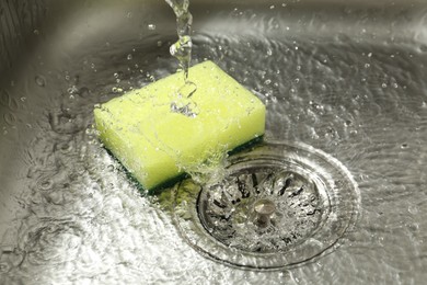 Photo of Water going down drain and sponge in sink, closeup