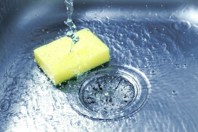Photo of Water going down drain and sponge in sink, closeup