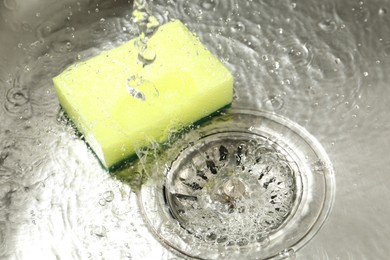 Photo of Water going down drain and sponge in sink, closeup