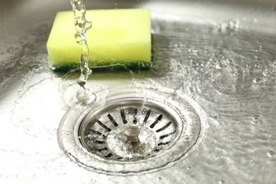 Photo of Water going down drain and sponge in sink, closeup