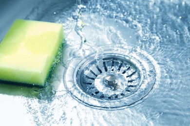 Photo of Water going down drain and sponge in sink, closeup