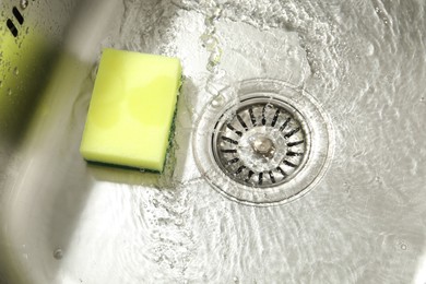 Photo of Water going down drain and sponge in sink, closeup