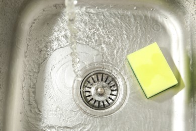 Photo of Water going down drain and sponge in sink, top view