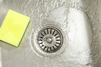 Photo of Water going down drain and sponge in sink, top view
