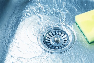 Photo of Water going down drain and sponge in sink, closeup