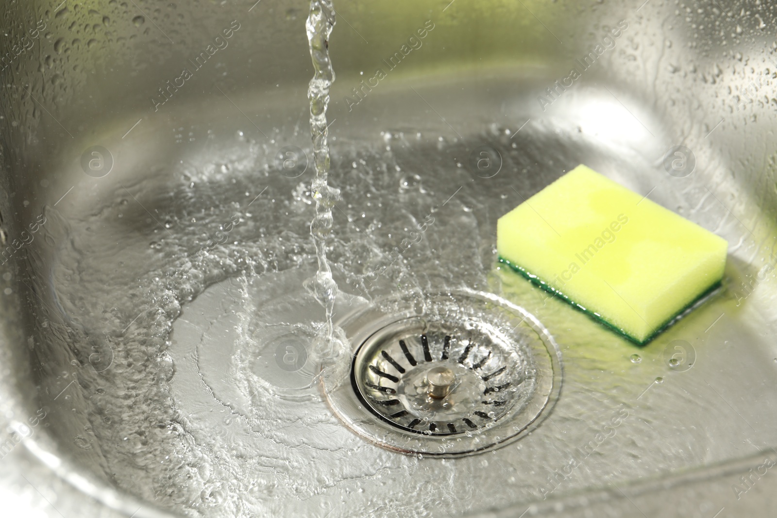 Water going down drain and sponge in sink, closeup Photo of Water going down drain and sponge in sink, closeup