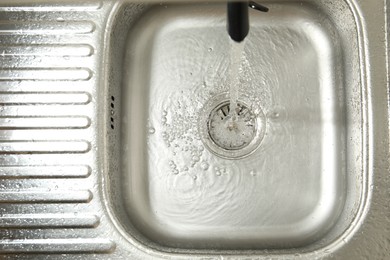 Photo of Water flowing from tap into sink, top view