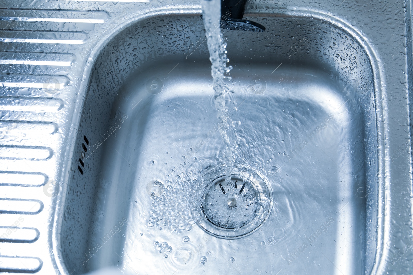 Water flowing from tap into sink, closeup Photo of Water flowing from tap into sink, closeup